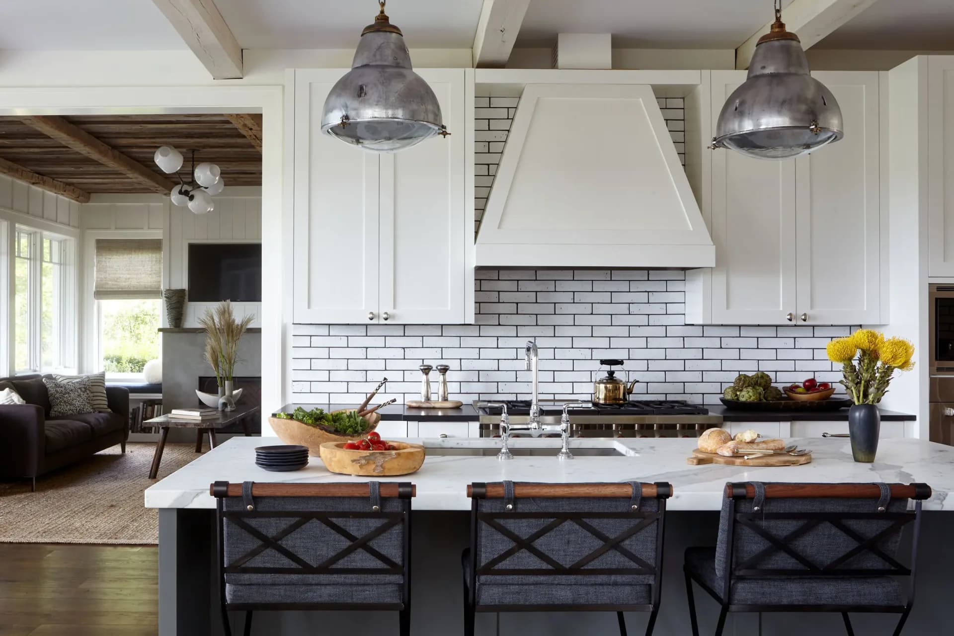 Modern kitchen with white cabinetry, subway tile backsplash, marble island with black stools, and industrial pendant lights by Jena White.