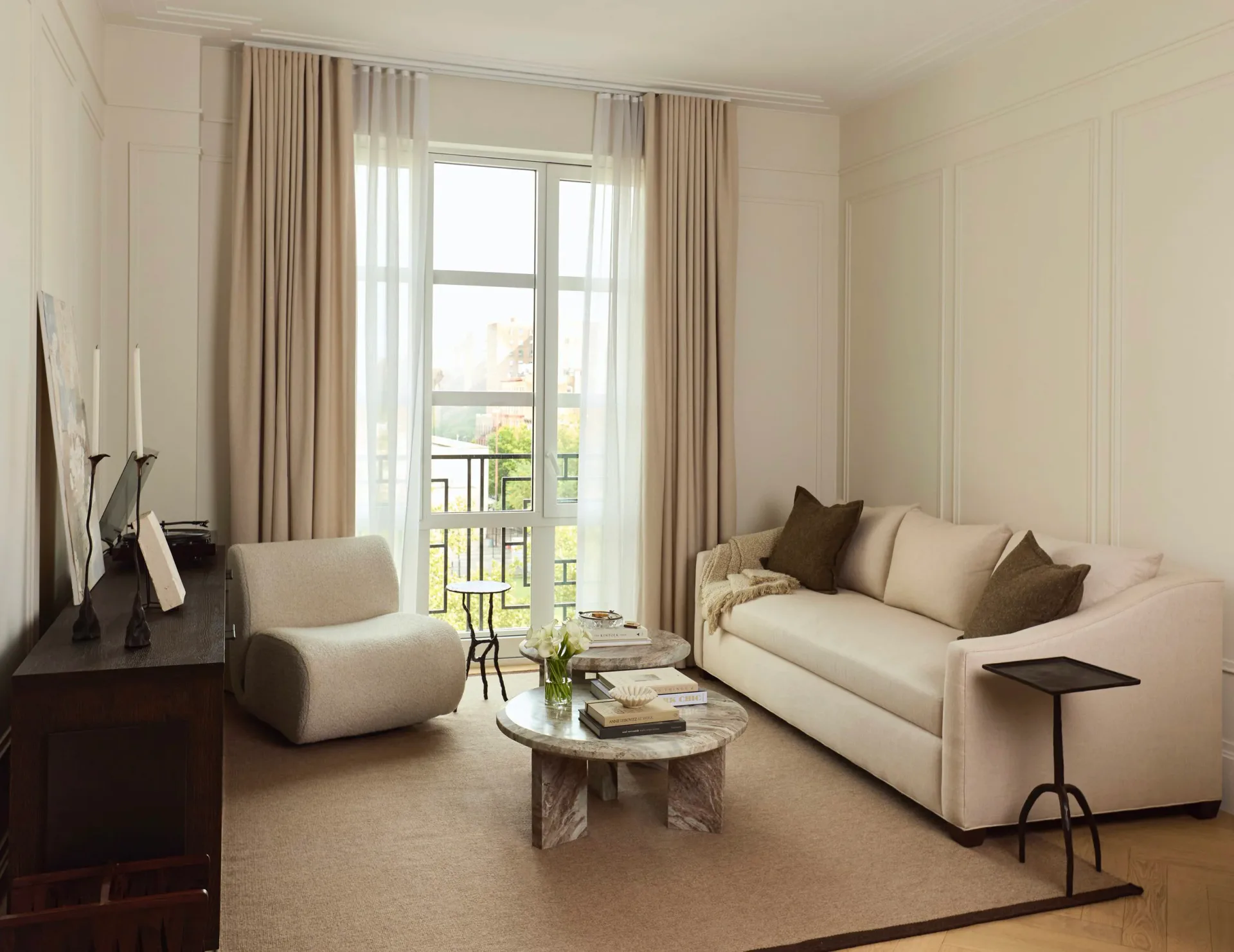 Bright, contemporary living room with cream sofa, neutral armchair, and glass coffee table facing French doors with floor-to-ceiling curtains by Jenna Reinero.