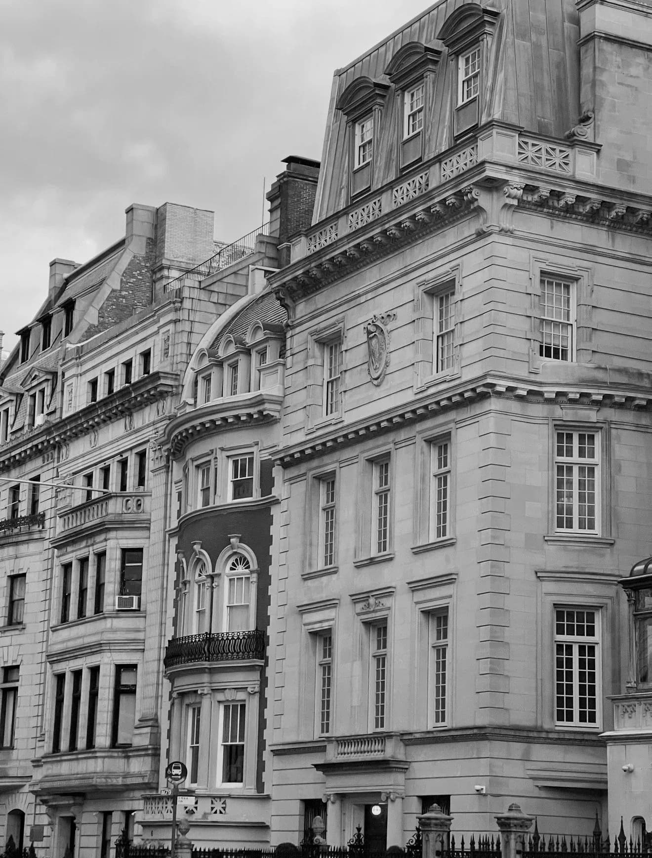 Classical stone facade with ornate architectural details, mansard roofs, and symmetrical fenestration in a monochromatic palette by Jennifer Paccione Angulo.
