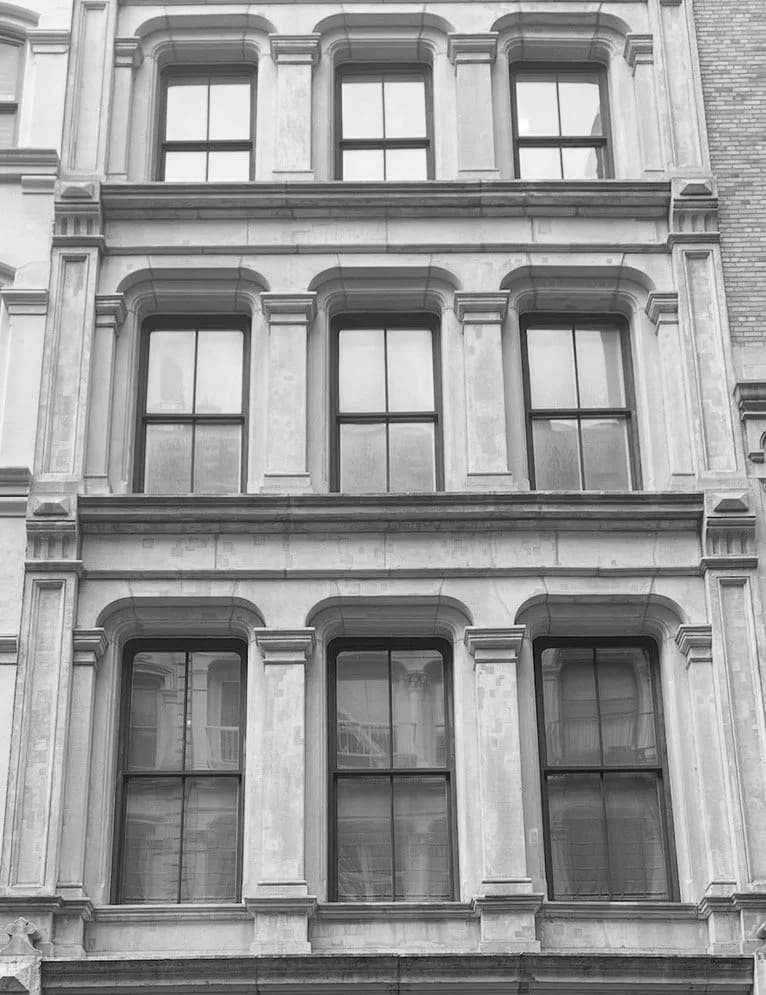 Symmetrical facade of a classical building with three stories of arched windows in stone and glass by Jennifer Paccione Angulo.