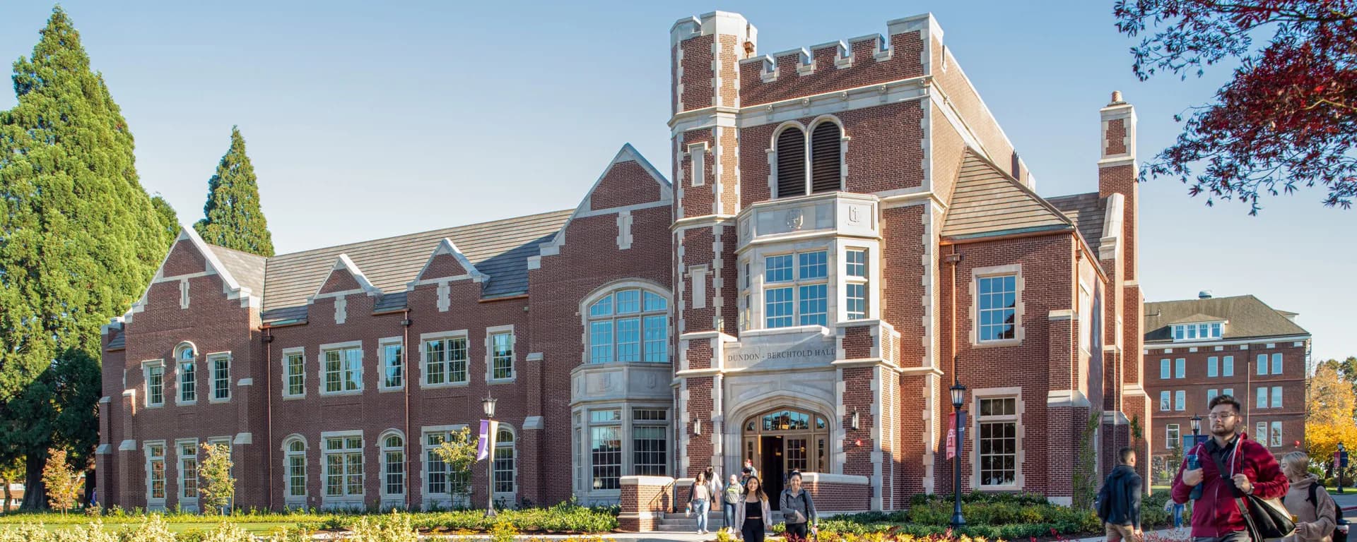 Red brick institutional building with Gothic Revival architecture, featuring arched windows, turrets, and manicured landscaping by Jennifer Stone