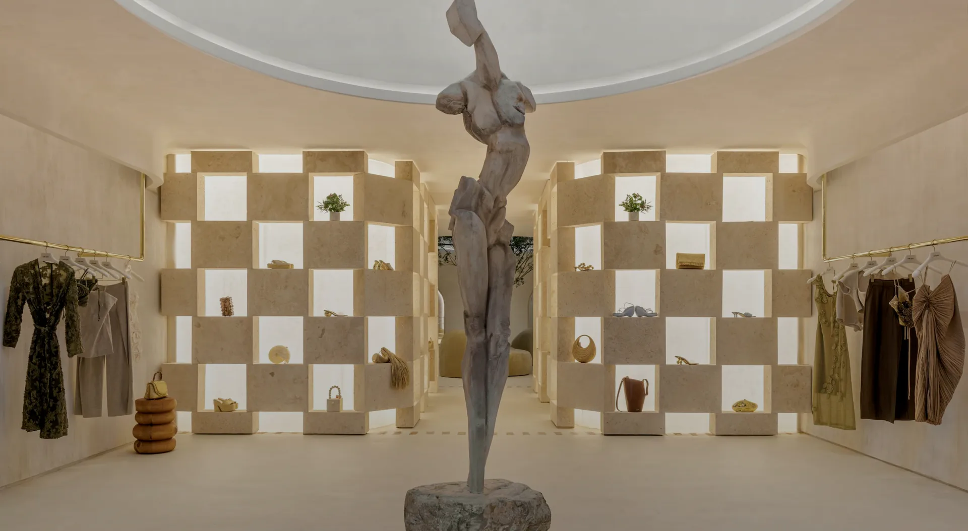 Minimalist retail interior with checkered tan and white wall display, central bronze sculptural figure, and clothing racks, designed by Jess Nahon.
