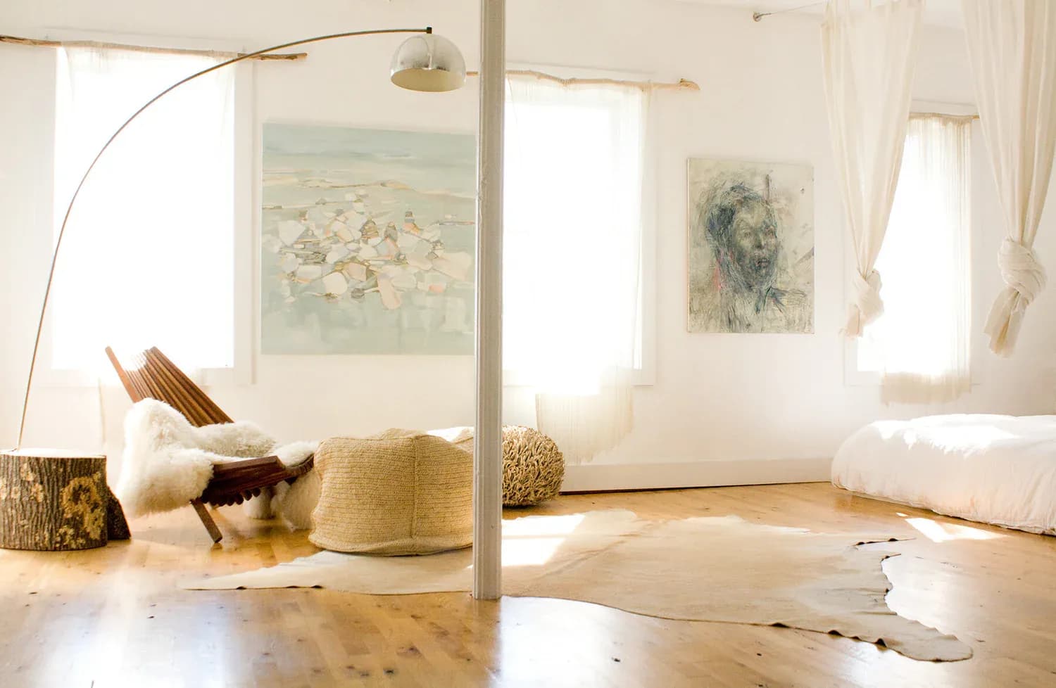 Minimalist interior space with light wood flooring, white walls, arched floor lamp, and framed artwork, designed by Jesse Elliott.