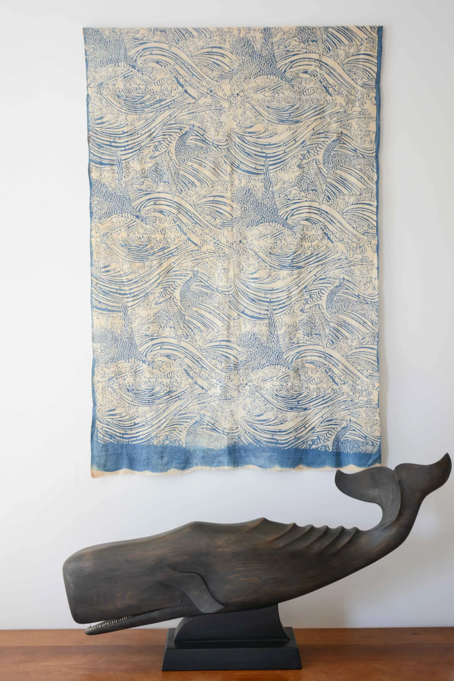 Contemporary interior styling featuring a carved wooden whale sculpture on a black base paired with a blue and cream patterned textile wall hanging by Jesse Elliott.