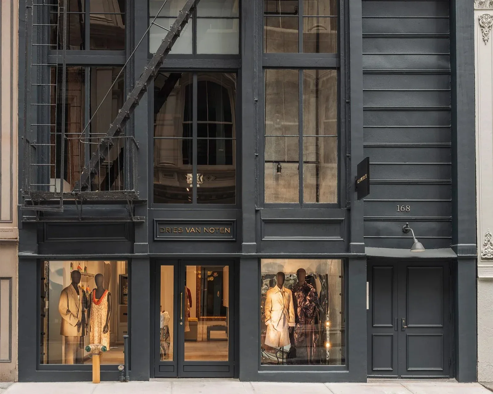 Dark charcoal storefront facade with large display windows showcasing clothing displays, featuring minimalist framing and vertical slatted elements by Jessica Hyland.