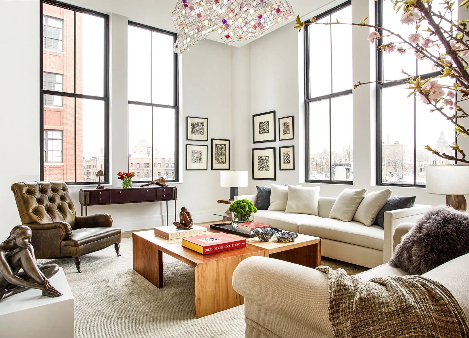 Bright loft living room with large windows, cream sofa, tufted gold chair, wooden coffee table, and botanical artwork by Jessica Law.
