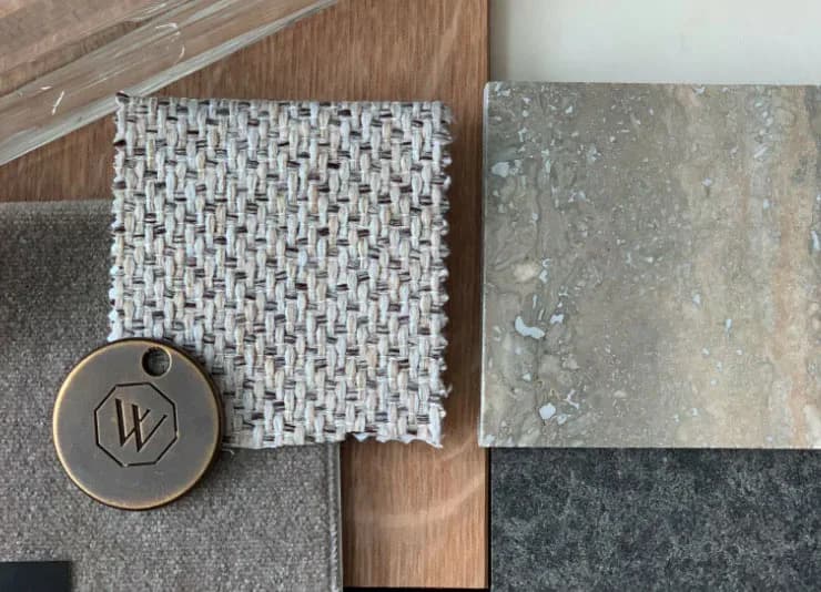 Material samples and finishes palette featuring white textured tile, concrete, wood grain, and dark stone arranged with a branded metal tag by Jessica Law.