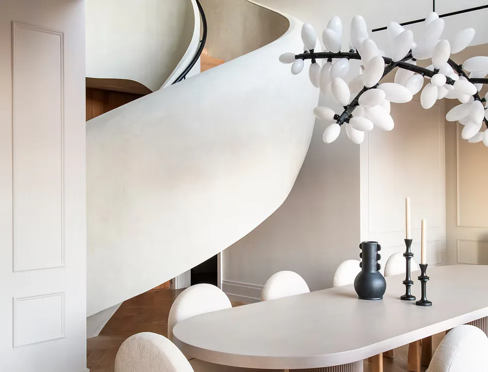 Modern dining room with sculptural white pendant light, curved white table, cream upholstered chairs, and decorative branch installation by Jessica Shaw.