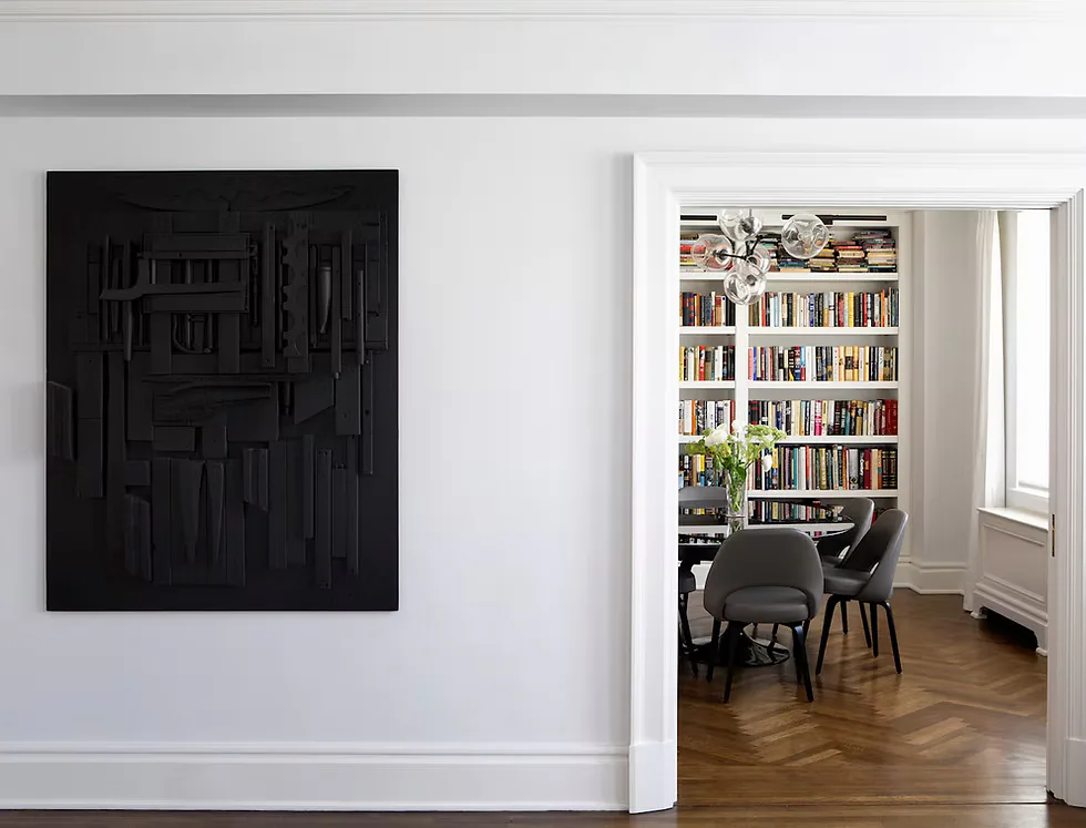 Modern living space featuring a black abstract textured artwork on white wall, with adjoining library room displaying floor-to-ceiling bookshelves, herringbone wood flooring, and mid-century seating by Jessica Shaw.