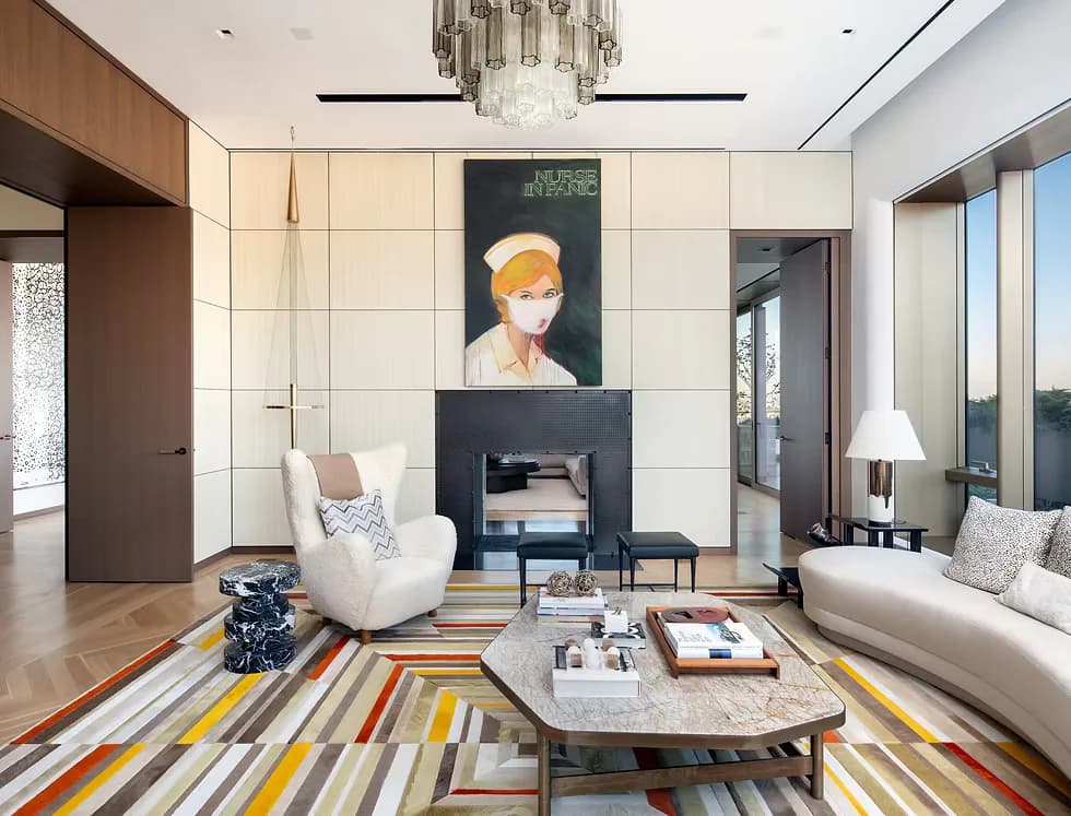 Modern living room with cream wall paneling, striped area rug in warm tones, curved white armchair, and fireplace feature wall designed by Jessica Shaw.