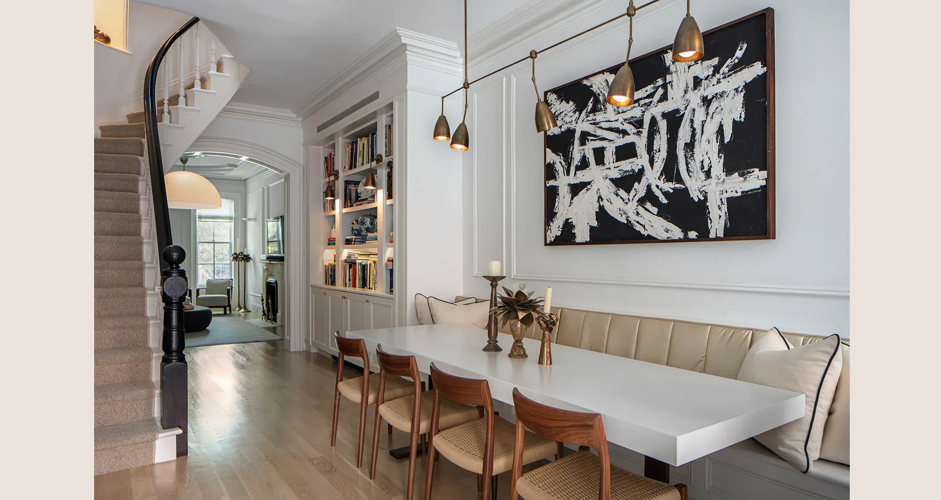 Modern dining room with white banquette seating, wooden chairs, pendant lights, and abstract black artwork, designed by Jessica Siegel.