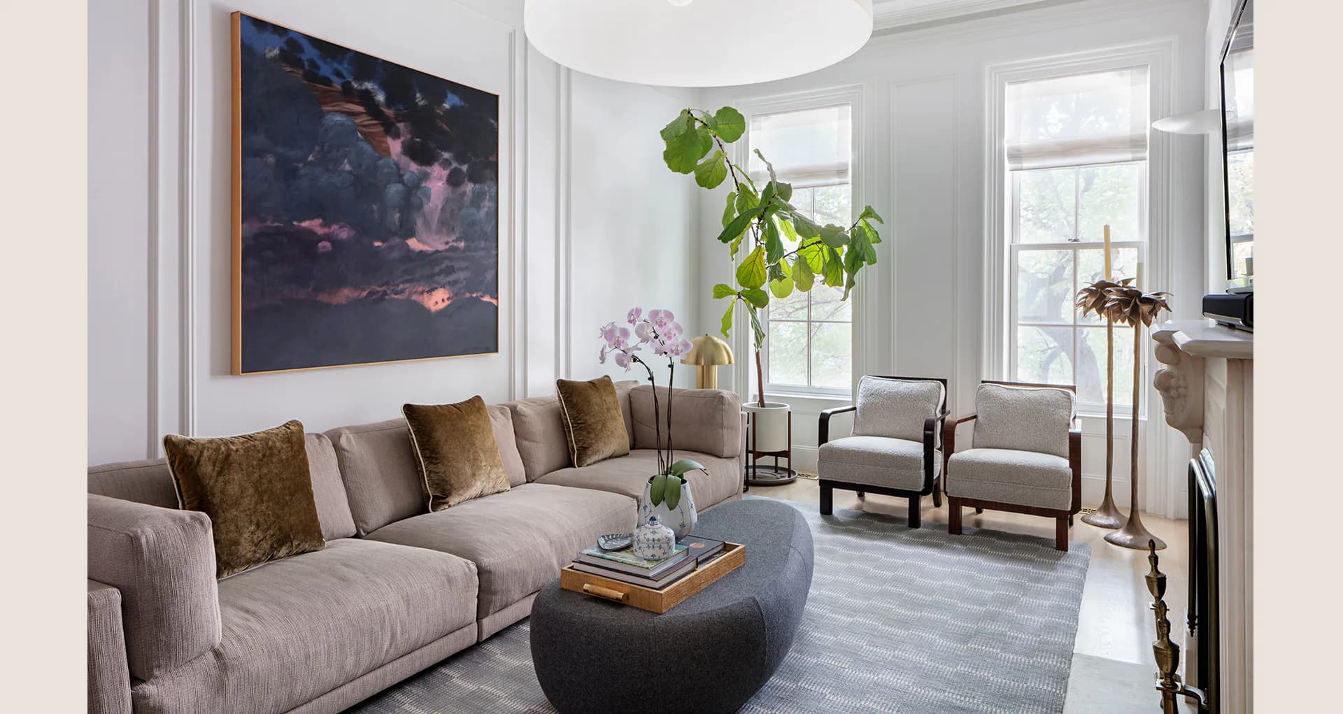A modern living room with a taupe sectional sofa, black round coffee table, and neutral palette accented with brass and natural wood, designed by Jessica Siegel.