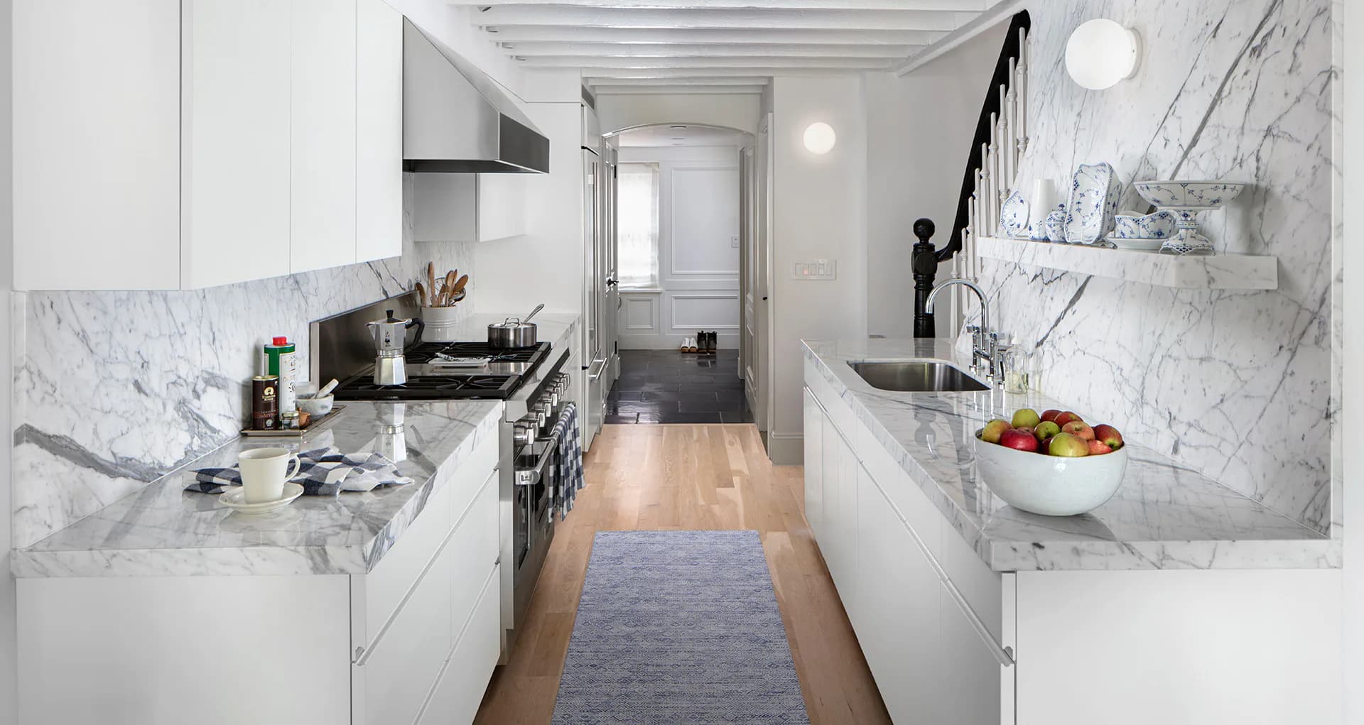 Marble galley kitchen with white cabinetry, integrated appliances, and marble backsplash by Jessica Siegel.
