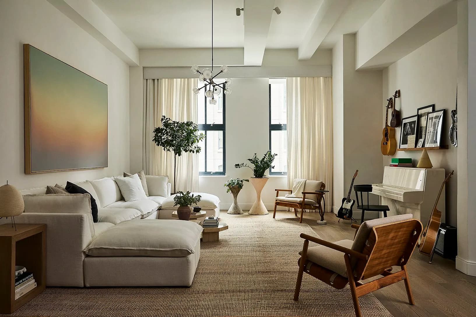 Modern living room with cream sofa, cognac leather chair, pendant lighting, and tall windows with cream curtains, neutral palette by Jessica Werner.