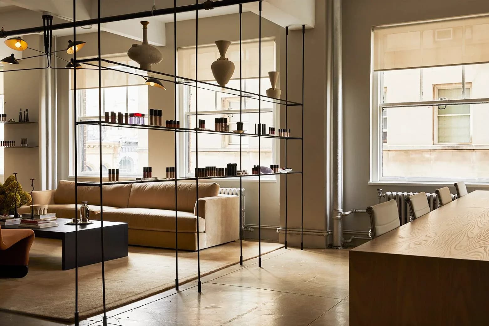 Modern retail interior with glass-enclosed shelving displaying products, warm wood tones, and sculptural pendant lighting, designed by Jessica Werner.