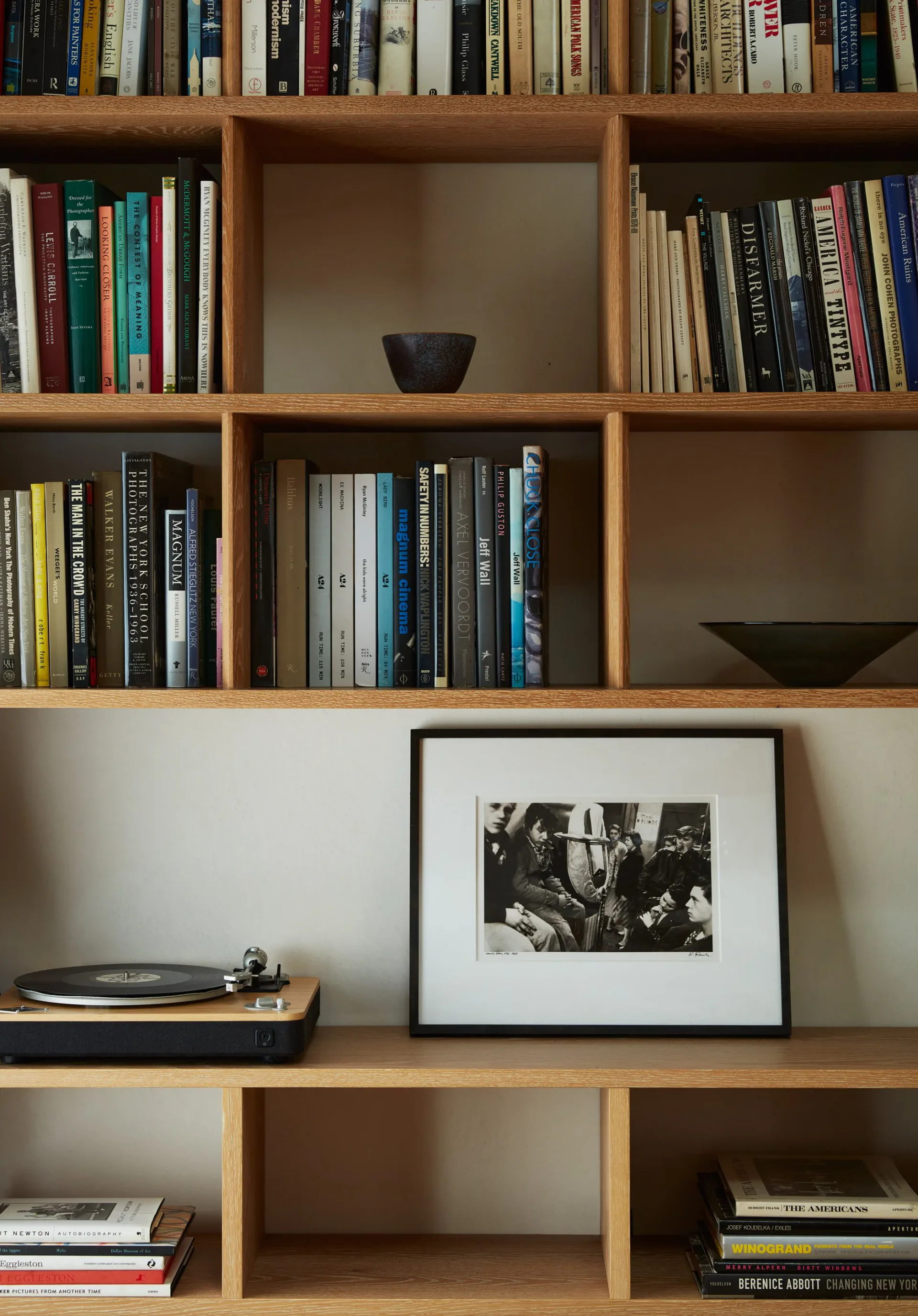 Custom wooden shelving unit with natural wood finish displaying books, a turntable, framed black-and-white photograph, and decorative bowls, designed by Jessie Childs.