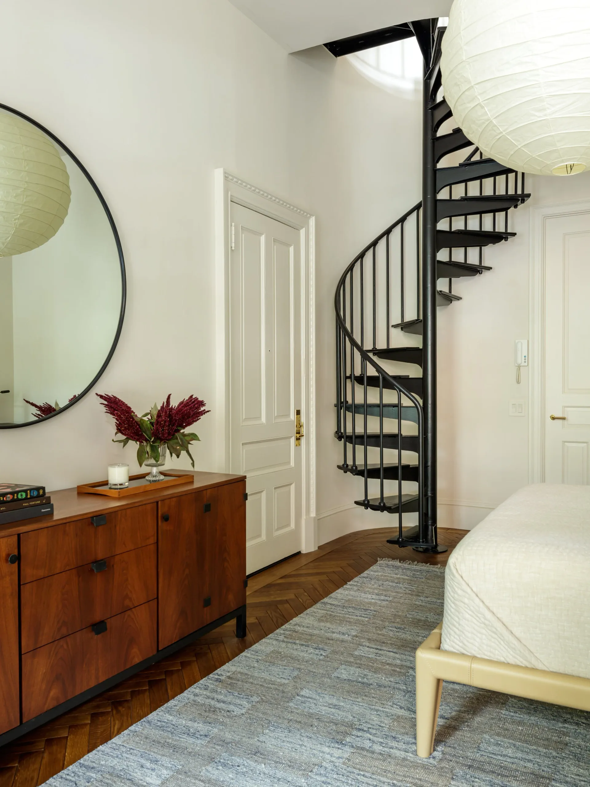 Modern bedroom with spiral staircase, wood dresser, round mirror, white doors, and pendant lighting by Jill Greenwood.