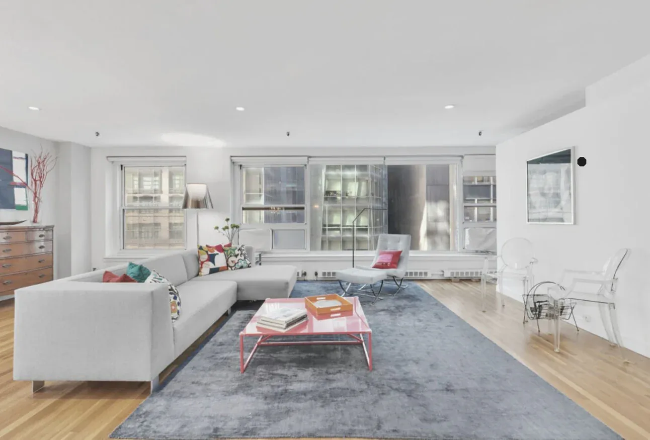 Modern living room with white sofa, gray area rug, and pink coffee table overlooking city windows, designed by Jo Laurie.