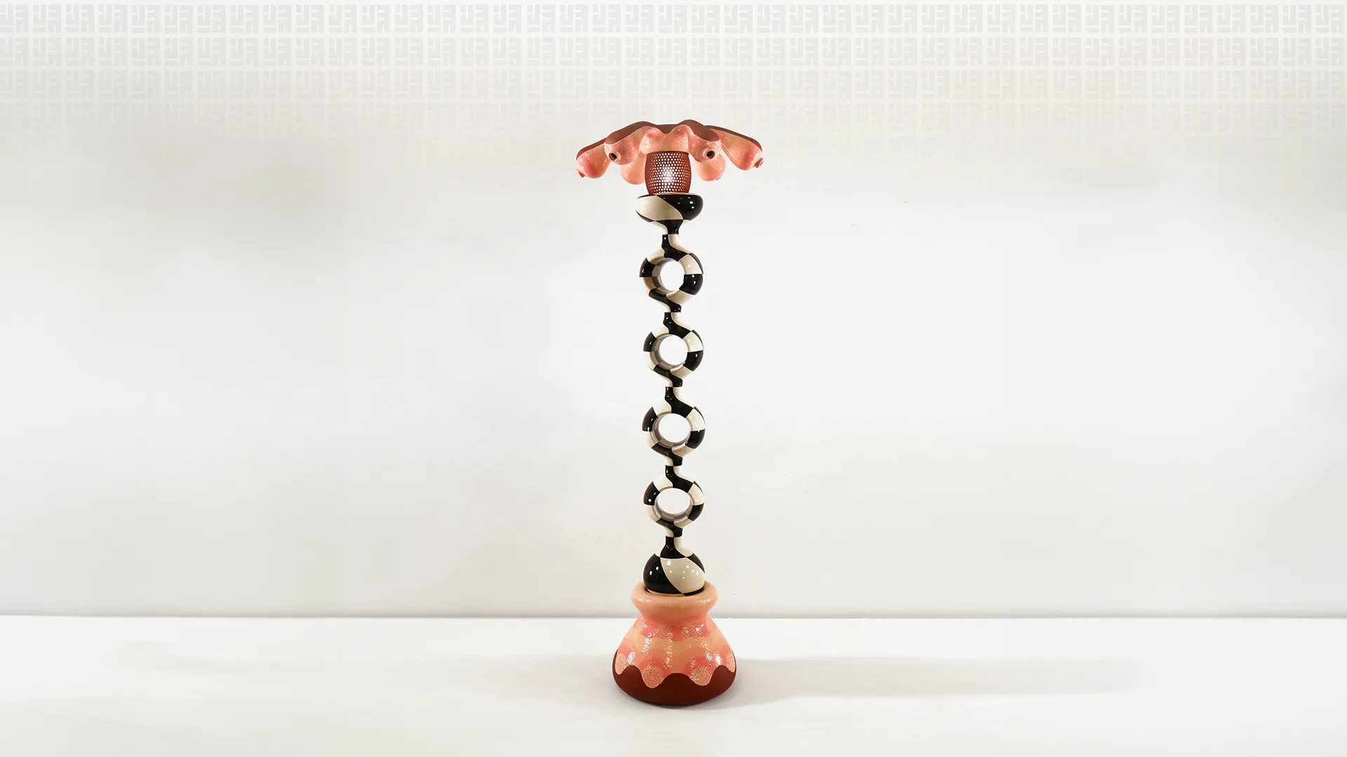 Sculptural object featuring copper-toned metallic elements stacked vertically with ornamental details, balanced composition against neutral background by Joël Brodovsky-Adams.
