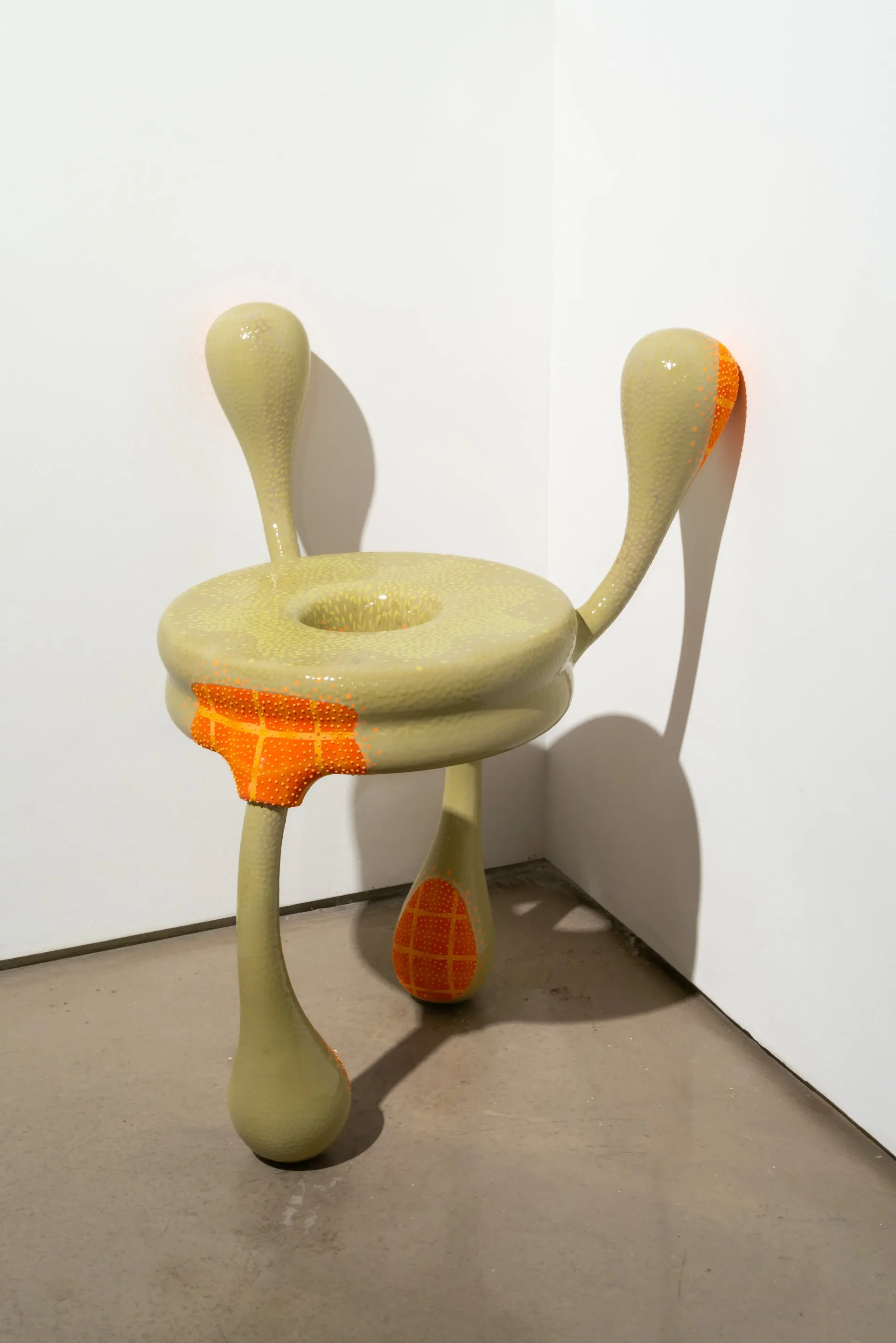 Sculptural furniture installation featuring pale yellow curved forms with orange textile accents arranged in a corner gallery space, by Joël Brodovsky-Adams.