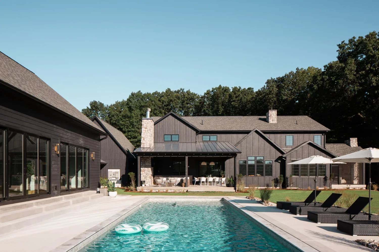 Modern residential exterior with heated swimming pool, limestone and dark wood facades, manicured lawn, and lounge seating by Johanna Tullis.