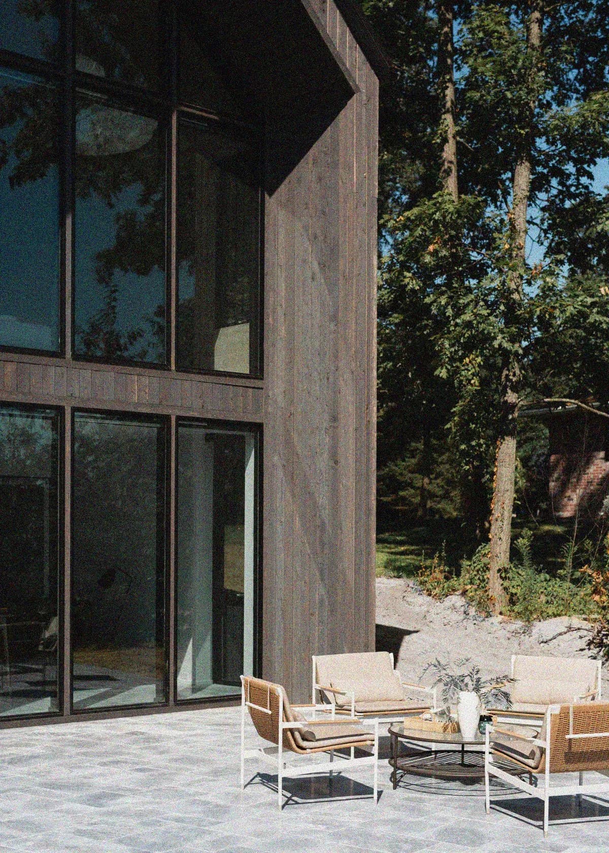 Modern exterior patio with dark wood cladding, large glazed doors, and mid-century furniture arrangement by Johanna Tullis.