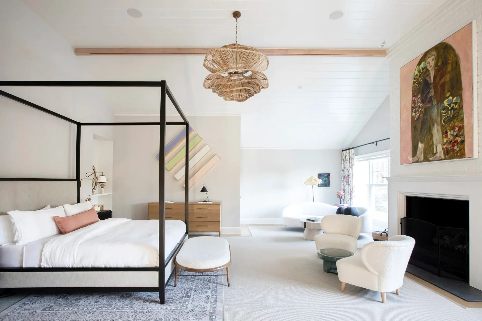 Serene primary bedroom with black canopy bed, natural wood nightstands, woven pendant light, fireplace, and neutral palette by John Bjornen.