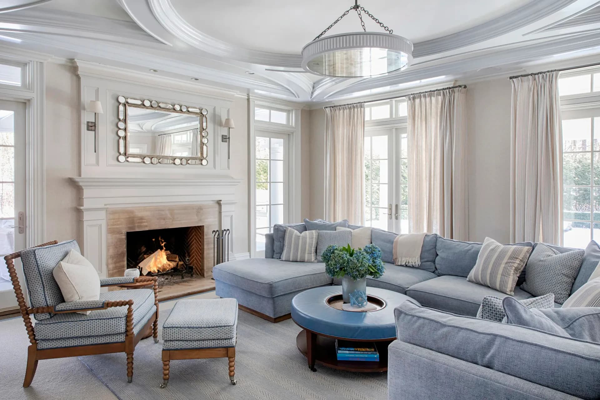 Elegant living room with fireplace, blue-gray sectional sofa, decorative pillows, round black coffee table, and formal seating by John Bjornen.