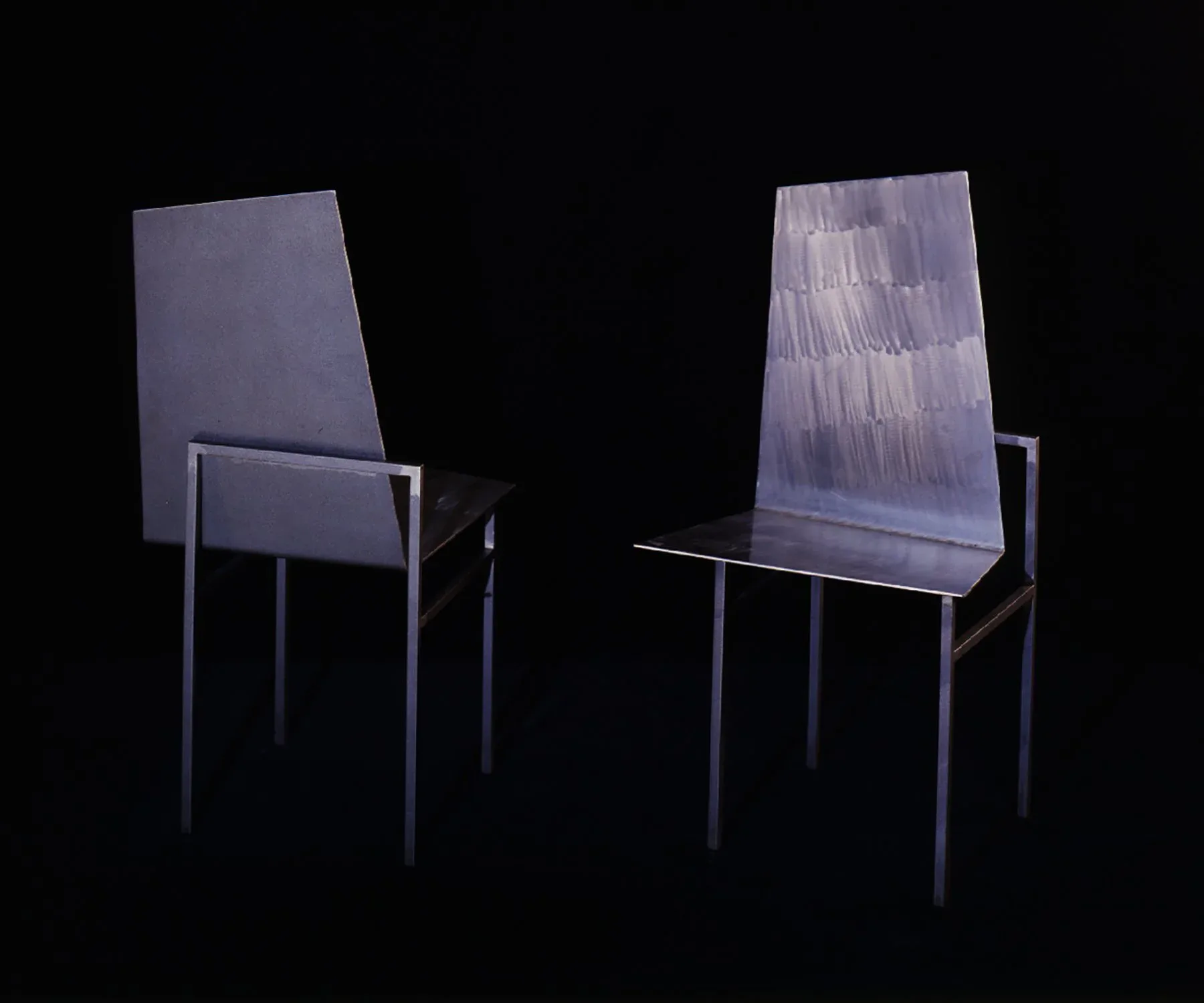 Two minimalist chairs with tall backrest panels rendered against black background, displaying subtle material texture and reflective surfaces by John Tinmouth.