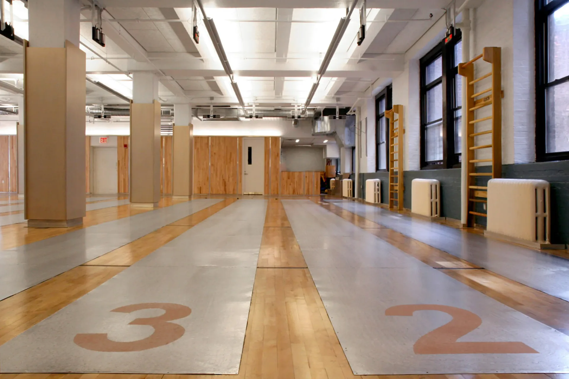Spacious studio or gymnasium with polished concrete floors, wooden lane dividers numbered 2 and 3, large windows, and industrial ceiling by John Tinmouth.