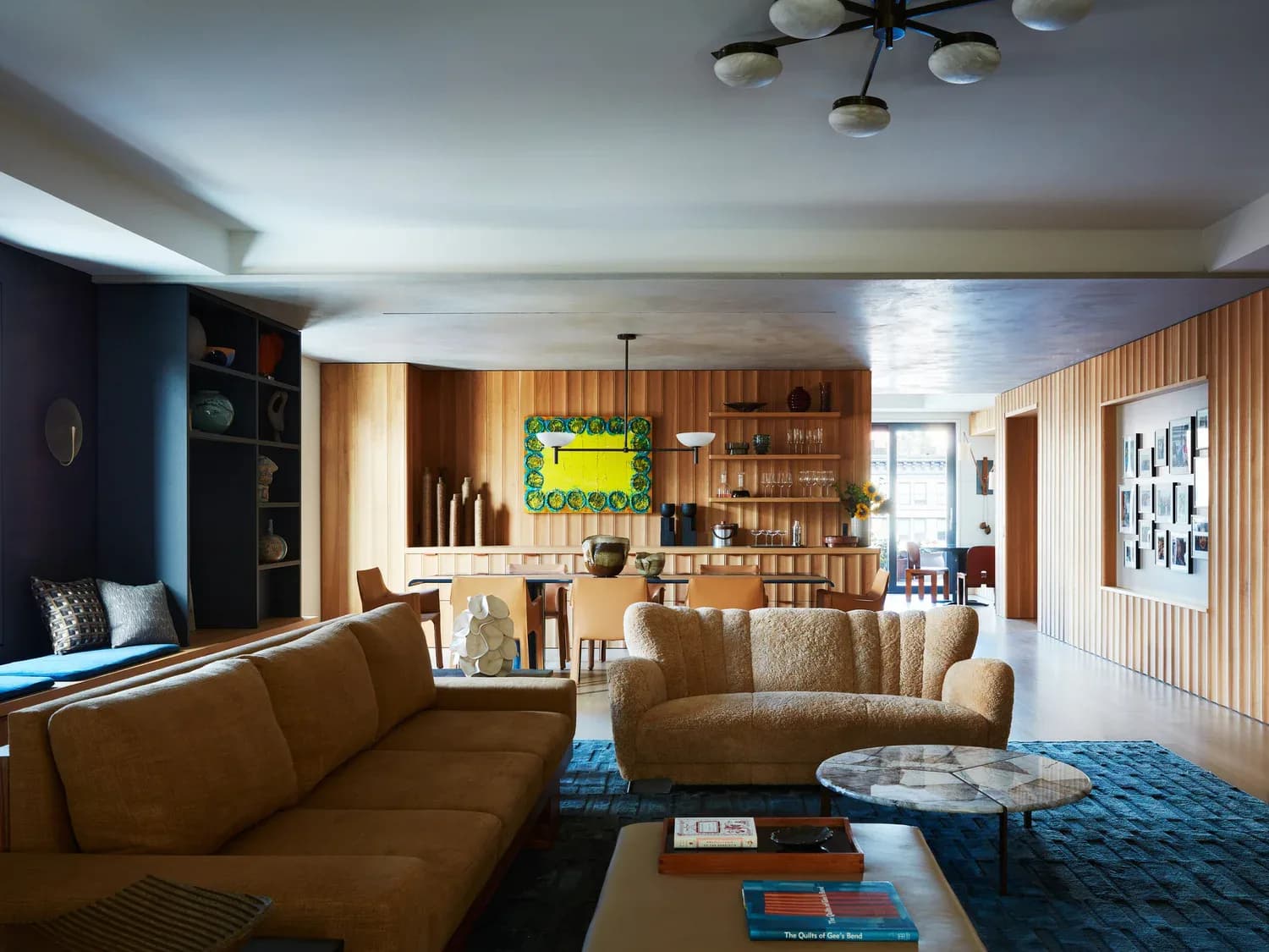 Contemporary living room with caramel leather seating, wood paneling, blue area rug, and built-in shelving by Jonah Kilday.