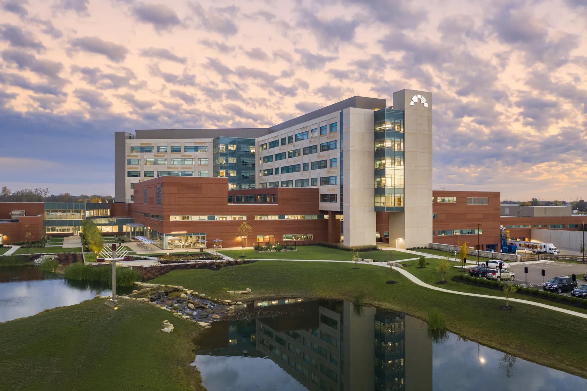 Modern institutional building with brick and glass facades reflected in a pond, surrounded by manicured lawn and contemporary landscaping by Jonathan Bykowski.