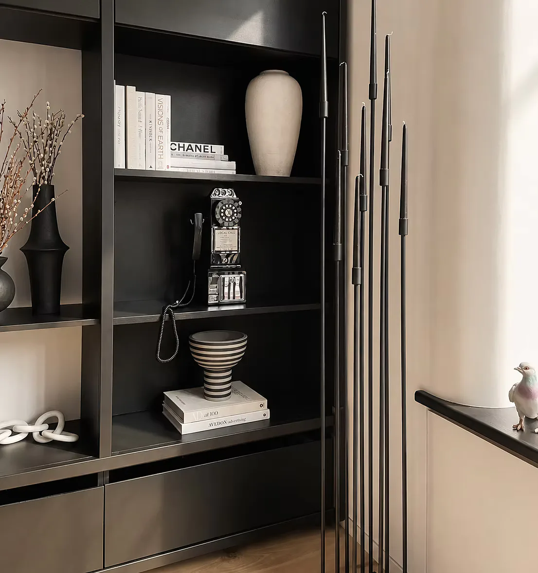 Modern black shelving unit with white ceramic vase, stacked books, striped bowl, and decorative objects against neutral wall, designed by Jordan Jones.