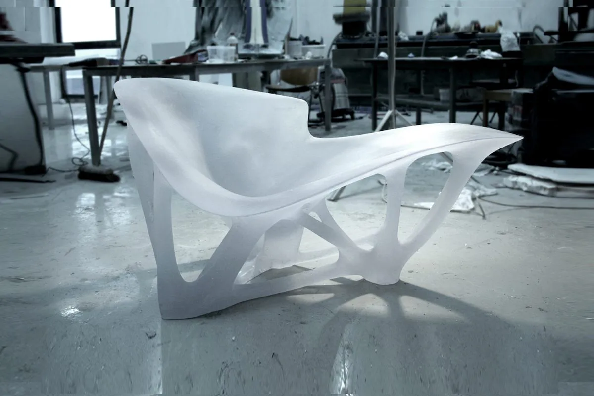 White sculptural chaise lounge with organic, flowing curves displayed in an industrial studio setting by Joris Laarman.