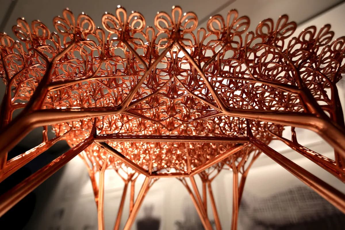 Intricate copper sculptural installation with organic, tree-like branching forms casting dramatic shadows against a white wall by Joris Laarman.