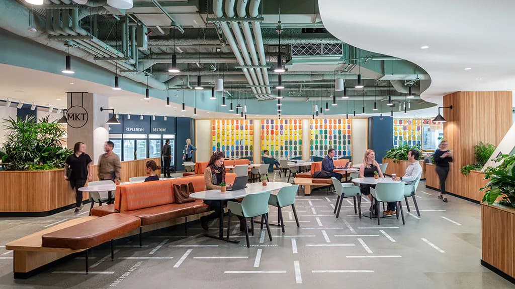 Modern office breakroom with turquoise ceiling, orange modular seating, wood paneling, and collaborative workspace by Joseph Brancato.