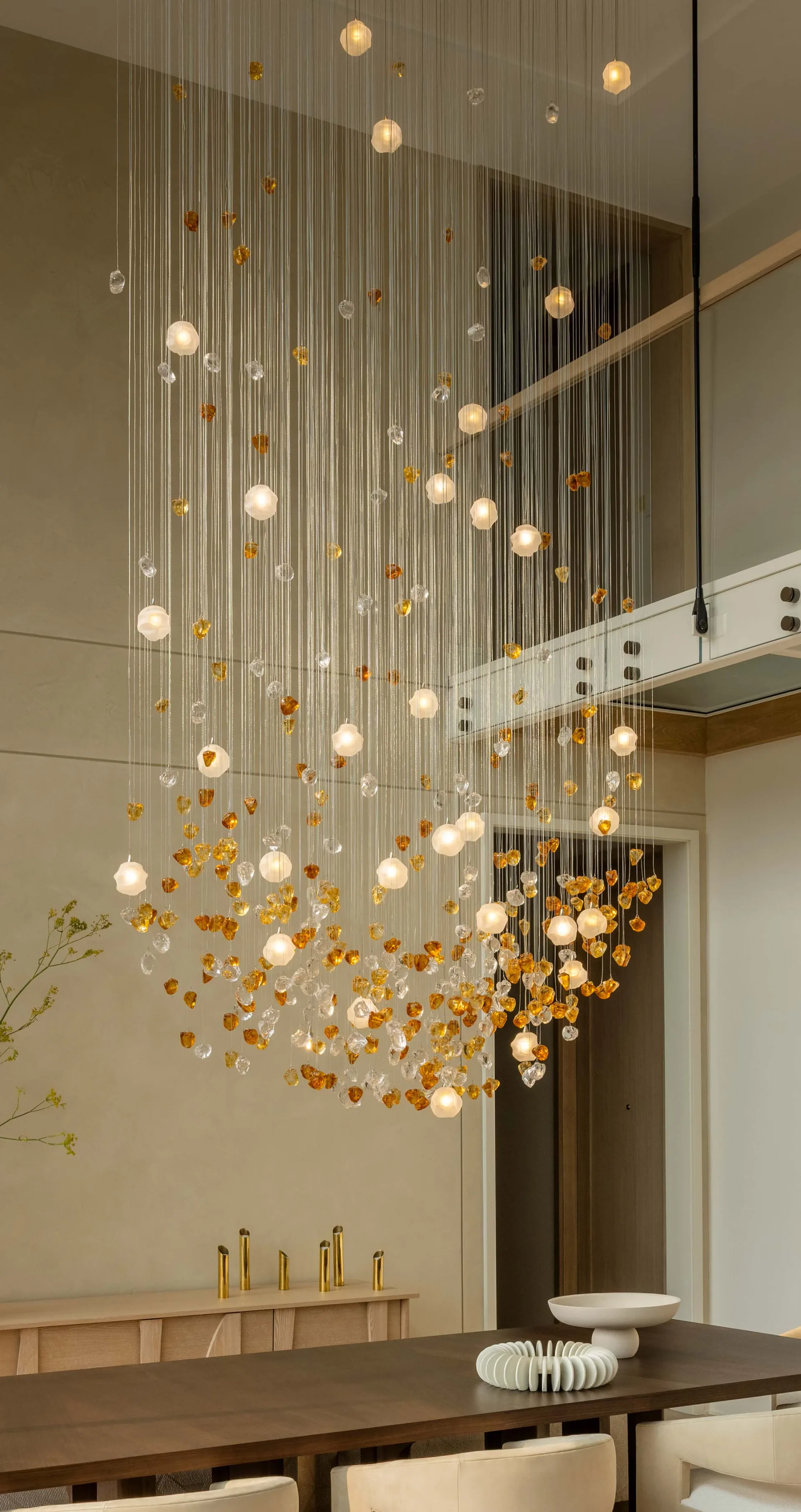 Modern dining space with sculptural pendant lighting installation featuring amber and frosted glass spheres suspended on thin wires by Joseph Sidof.