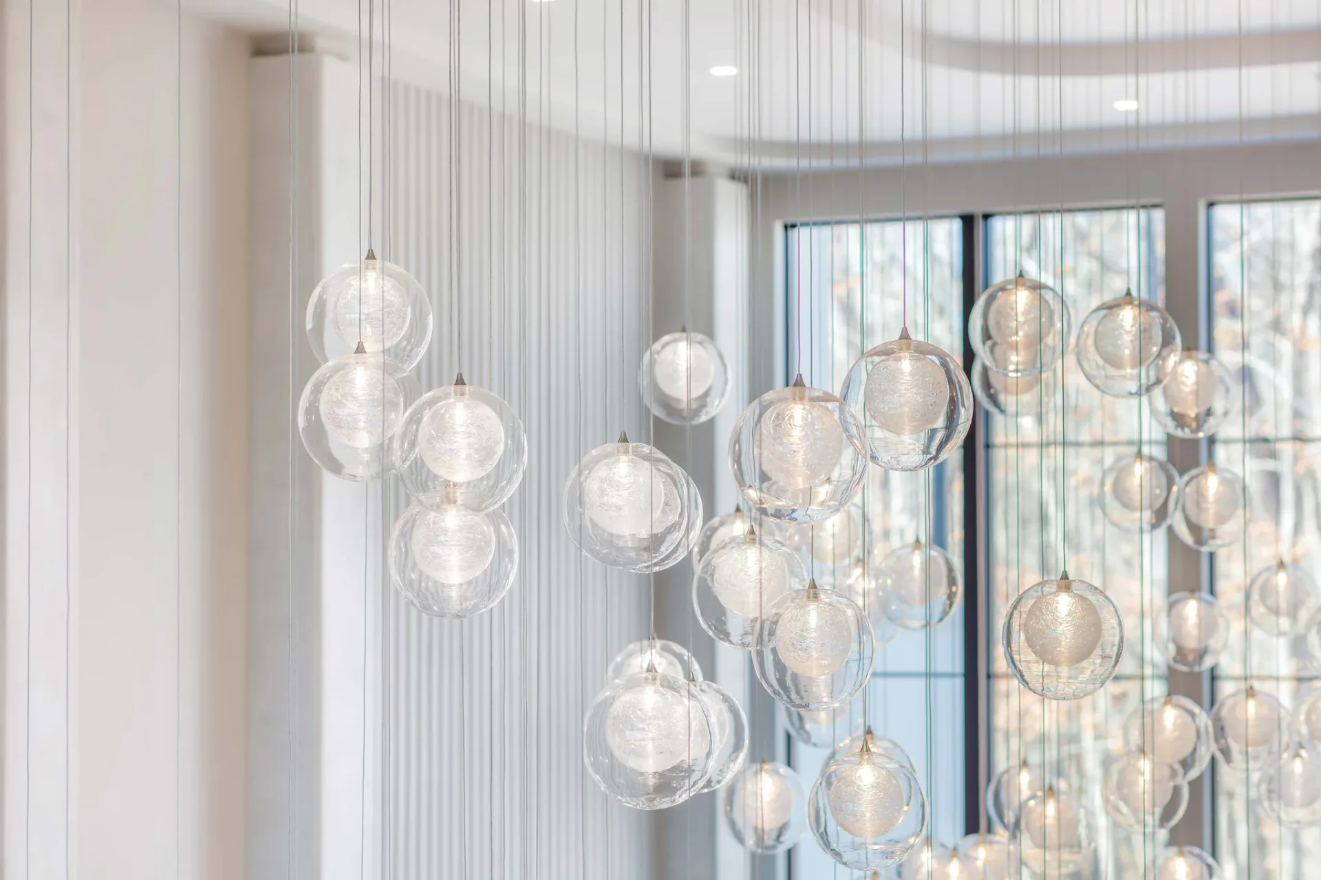 Modern pendant lighting installation with cascading glass spheres suspended from ceiling in bright, minimalist interior by Joseph Sidof.