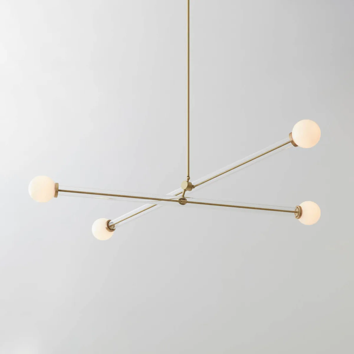 Brass mid-century modern pendant light fixture with cream-colored spherical shades extending from a central hub, suspended against neutral background by Josh Metersky.