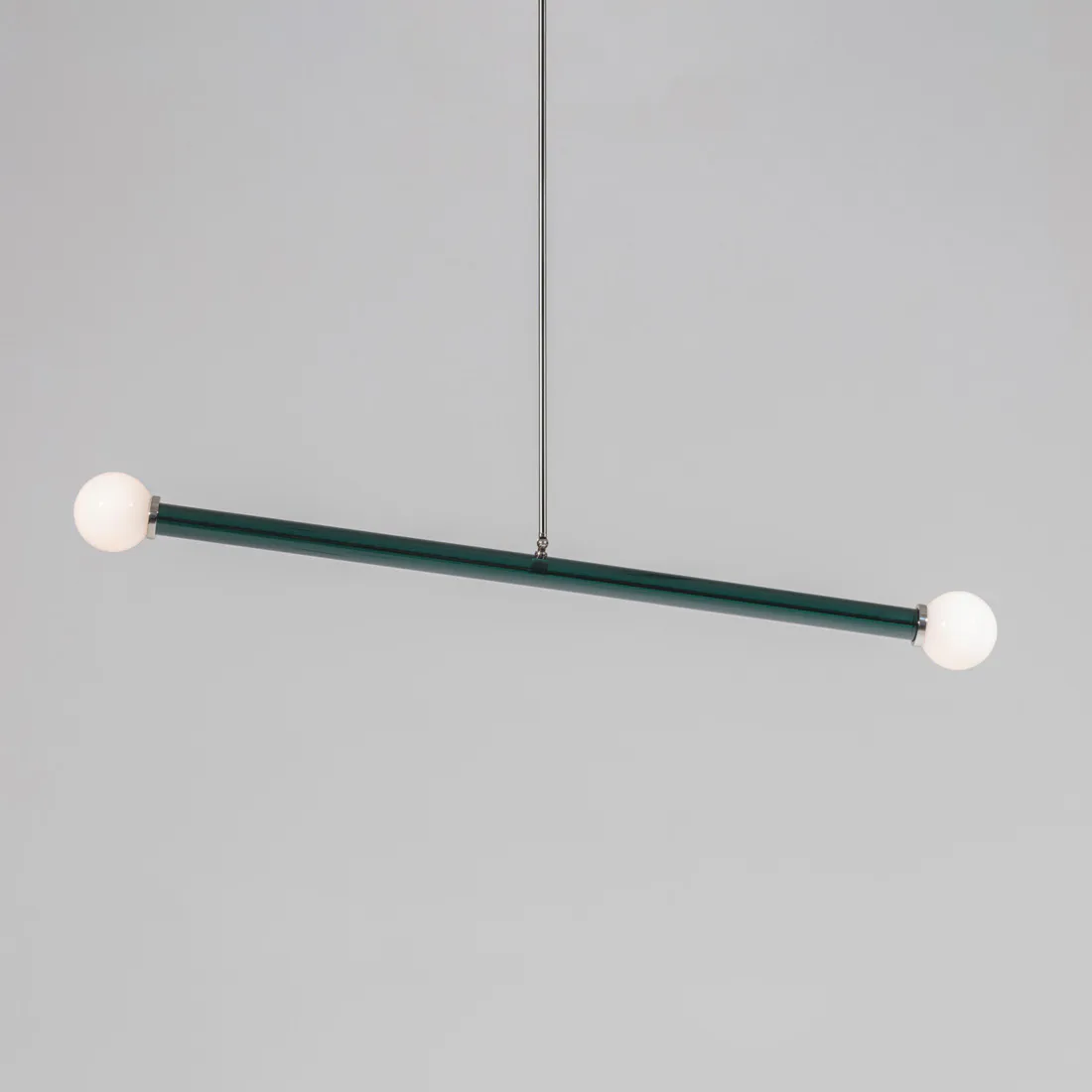 Minimalist pendant lighting fixture with teal metal rod suspended from wire, featuring white spherical orbs at each end, by Josh Metersky.
