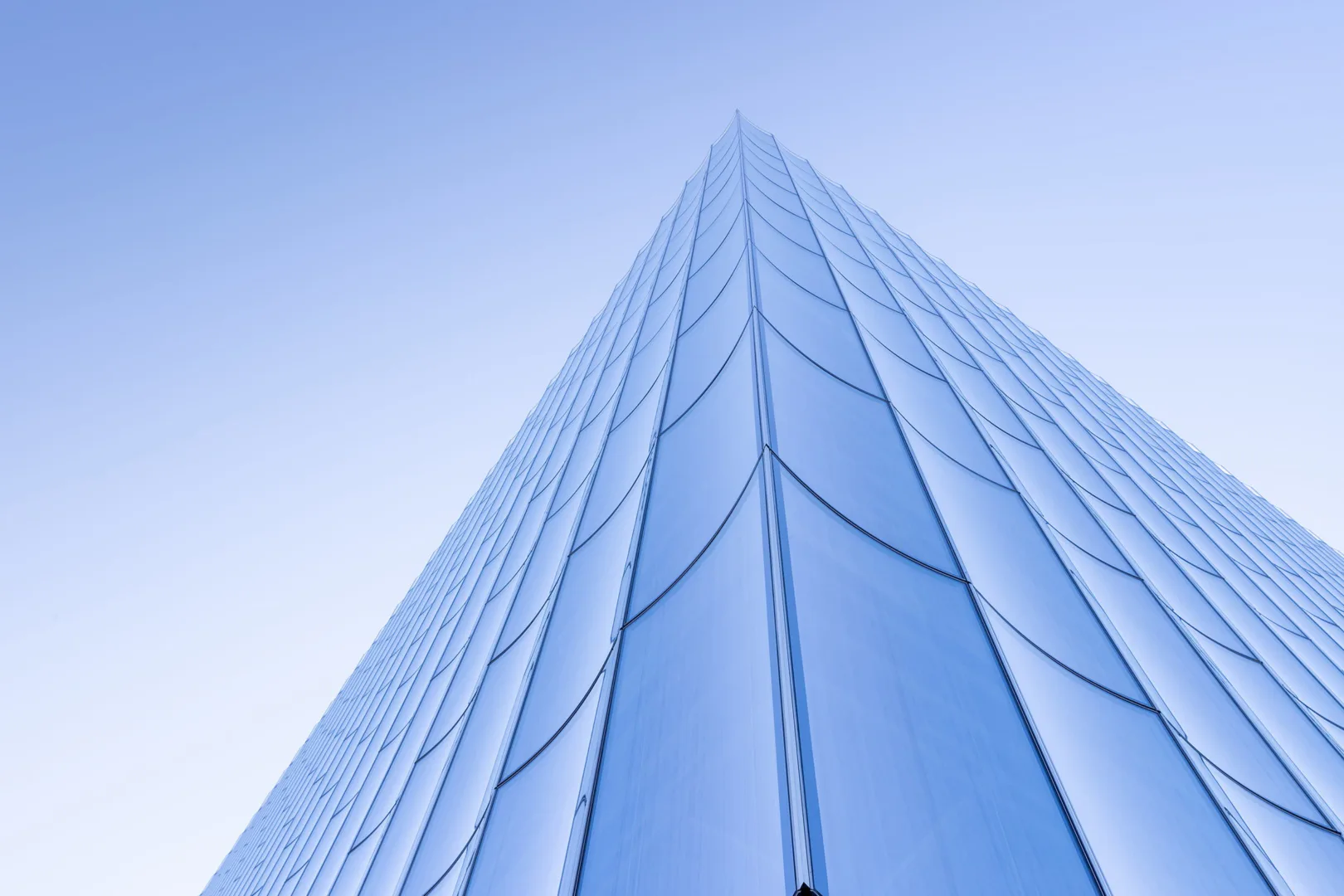 Soaring glass and steel tower facade photographed from below, featuring geometric vertical ribbing and blue-tinted curtain wall systems by Joshua Ramus.