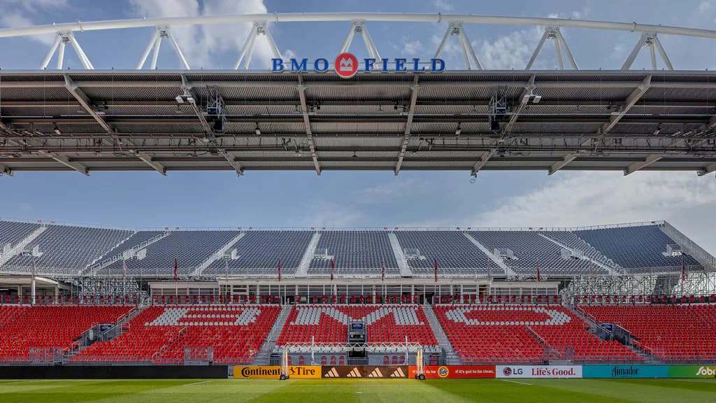 Modern stadium interior with red seat sections and structural steel framework under bright sky, designed by Ju Hyun Lee.