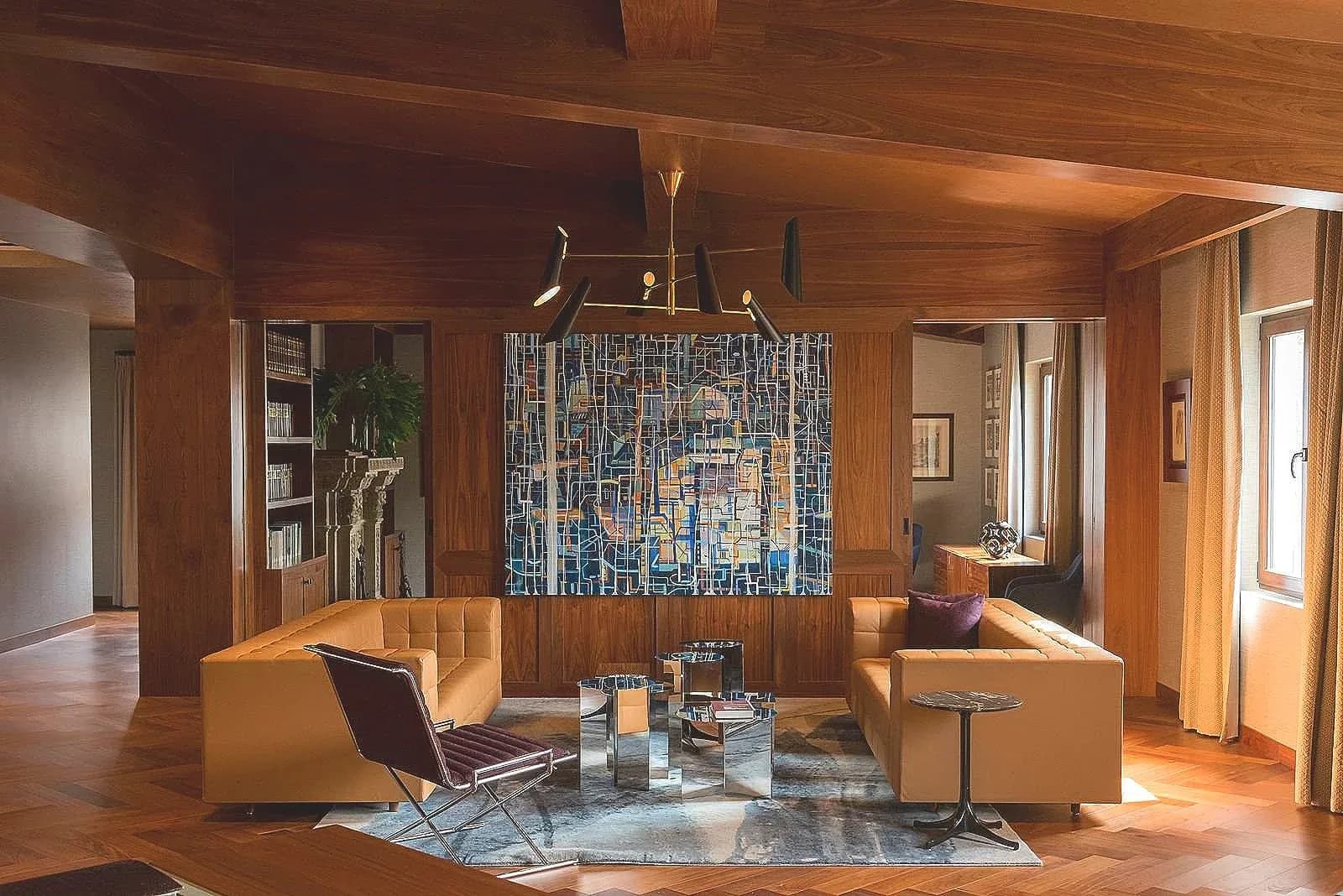 Warm wooden interior with modern seating arrangement, blue mosaic artwork, natural light, and minimalist furnishings by Juan J. Carretero.