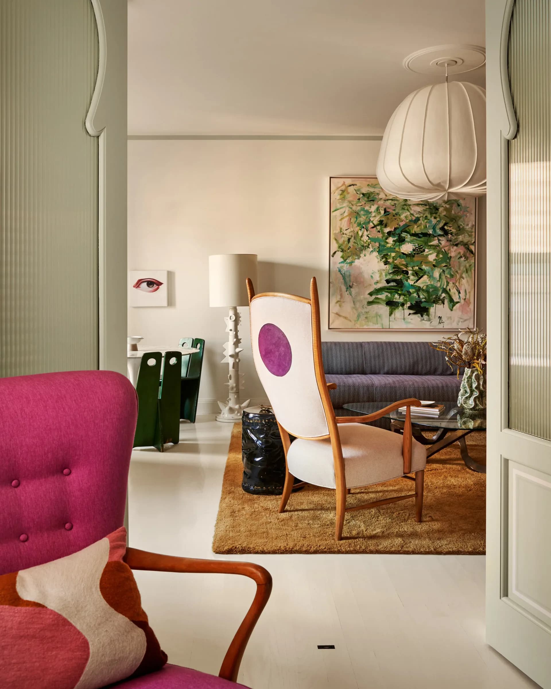 Modern interior with vibrant pink upholstered chair, wooden mid-century furniture, natural jute rug, and botanical artwork, designed by Juan J. Carretero.