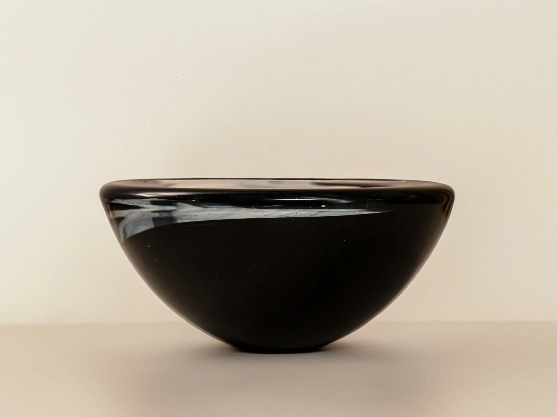 Black glossy ceramic bowl with curved hemispherical form and polished rim, displayed against neutral background by Juan Russo.