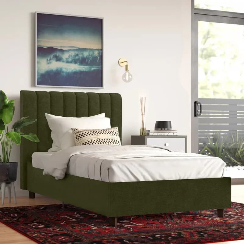 Modern bedroom with olive green upholstered bed, white bedding, and patterned pillows, featuring a landscape artwork above the headboard and burgundy area rug, designed by Juanita Jimenez.