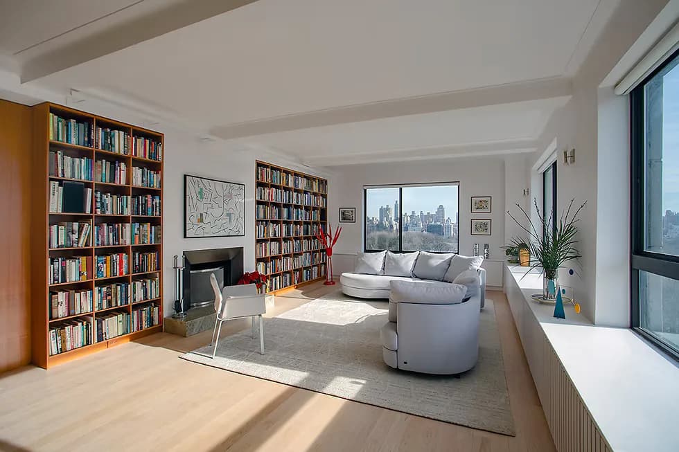 Bright, modern living room with wood shelving, fireplace, curved gray seating, and city views, featuring clean lines and minimalist décor by Judith Gerrard.