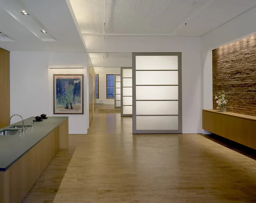 Modern gallery reception area with warm wood flooring, minimalist cabinetry, and frosted glass entry door by Judith Gerrard.