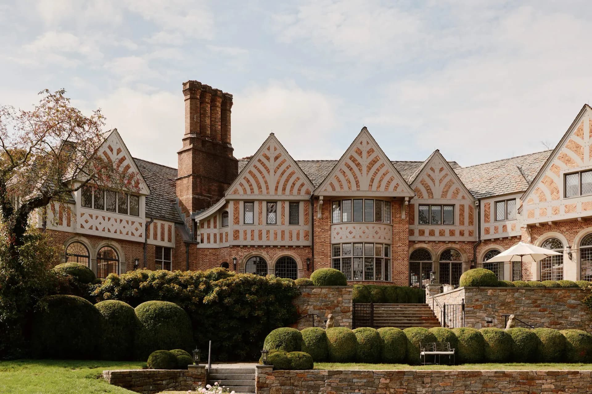 Tudor-style brick mansion with decorative half-timbering, multiple gables, and manicured hedges designed by Judith Limon.