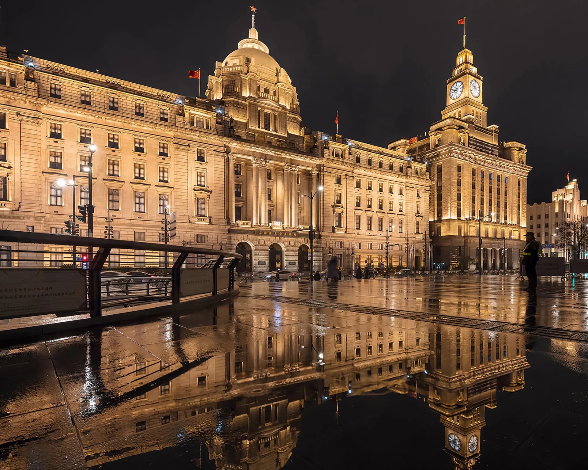 Illuminated neoclassical buildings reflected in wet pavement at night, architectural lighting design by Jules Fisher.